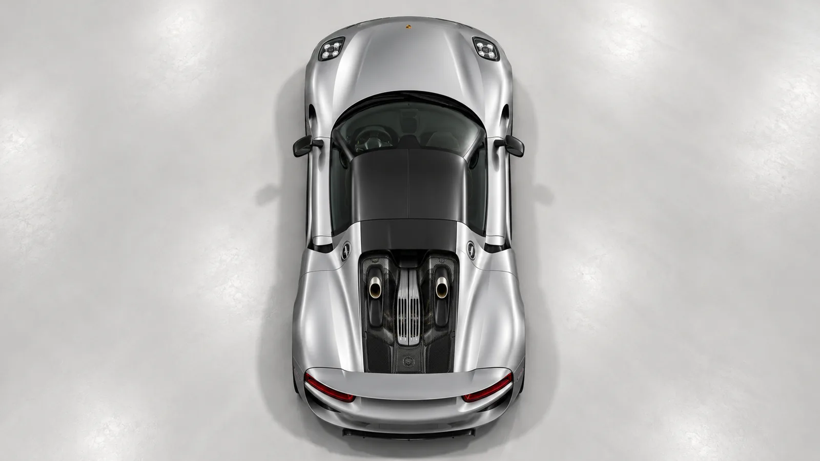 The silver Porsche 918 Spyder viewed directly from above, revealing its black roof and symmetrical top-exit exhaust layout.